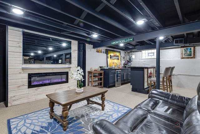 living room featuring wooden walls, beverage cooler, indoor wet bar, a glass covered fireplace, and speckled floor