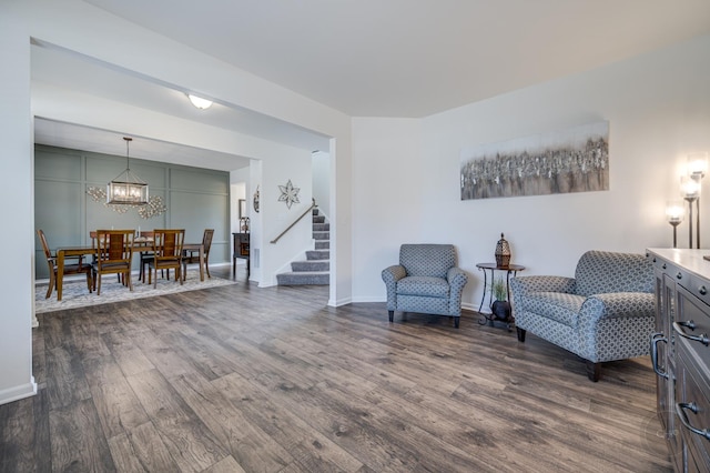 living area with stairway, baseboards, an inviting chandelier, and dark wood-style flooring