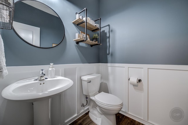 bathroom featuring toilet, wood finished floors, wainscoting, and a decorative wall