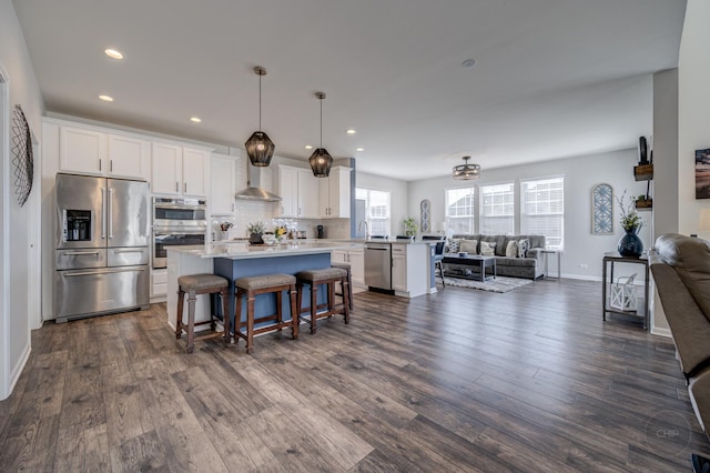 kitchen with dark wood-type flooring, wall chimney range hood, open floor plan, appliances with stainless steel finishes, and a kitchen breakfast bar