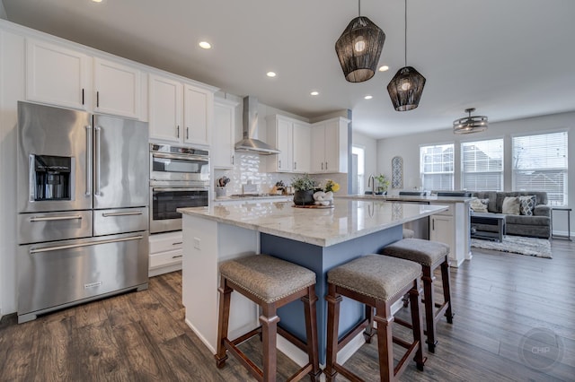 kitchen featuring a sink, stainless steel appliances, white cabinets, wall chimney range hood, and tasteful backsplash