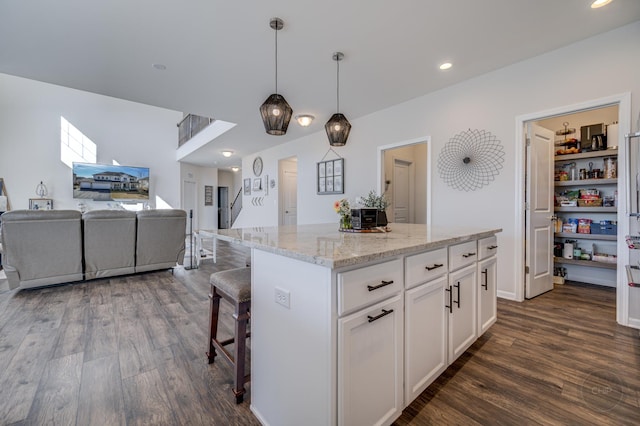 kitchen featuring a breakfast bar area, dark wood finished floors, white cabinets, decorative light fixtures, and a center island