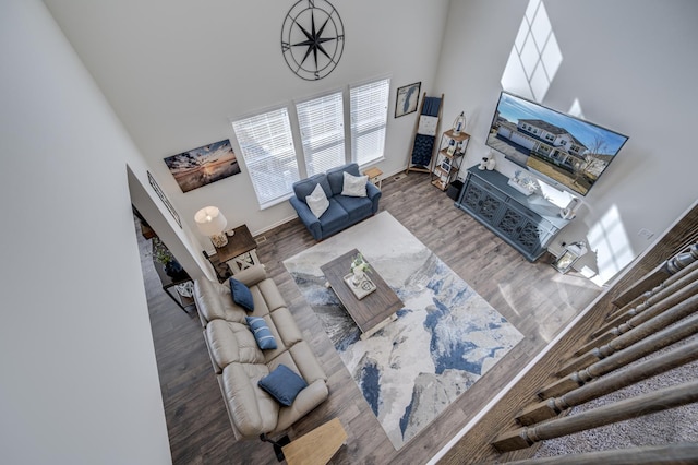 living area with baseboards, wood finished floors, and a towering ceiling