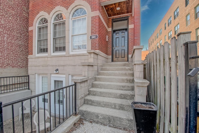 view of exterior entry featuring brick siding and fence