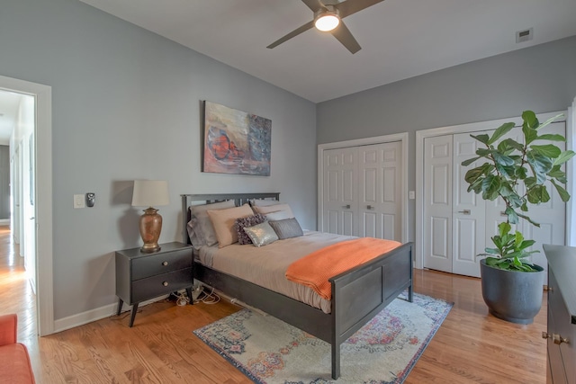 bedroom with baseboards, visible vents, light wood finished floors, and multiple closets