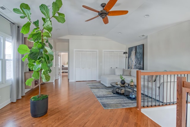 living area with visible vents, wood finished floors, a ceiling fan, and vaulted ceiling