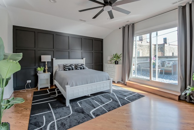 bedroom featuring visible vents, a ceiling fan, wood finished floors, a decorative wall, and vaulted ceiling