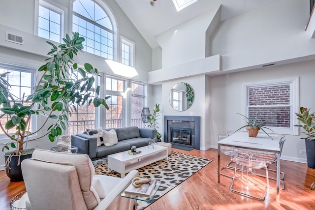 living room with a glass covered fireplace, visible vents, baseboards, and wood finished floors