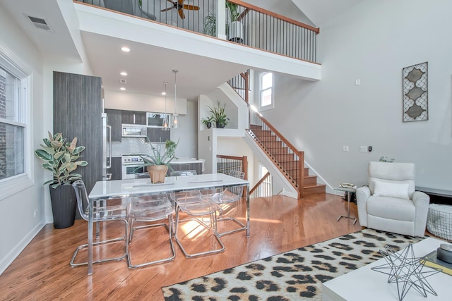 dining area featuring visible vents, baseboards, stairs, light wood-style floors, and a towering ceiling