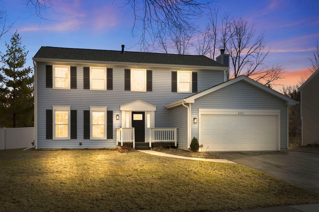 colonial house with fence, a yard, concrete driveway, a garage, and a chimney