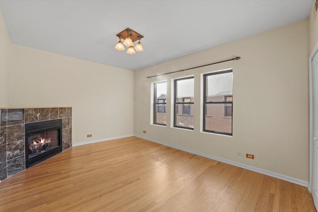 unfurnished living room with baseboards, wood finished floors, and a tile fireplace