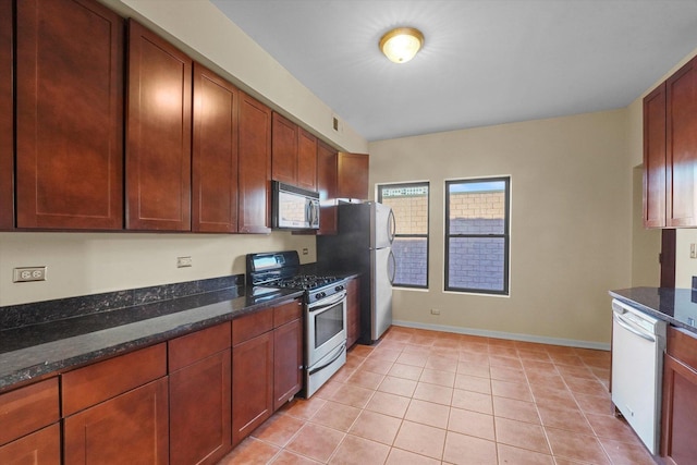 kitchen with light tile patterned floors, dark stone counters, baseboards, and appliances with stainless steel finishes