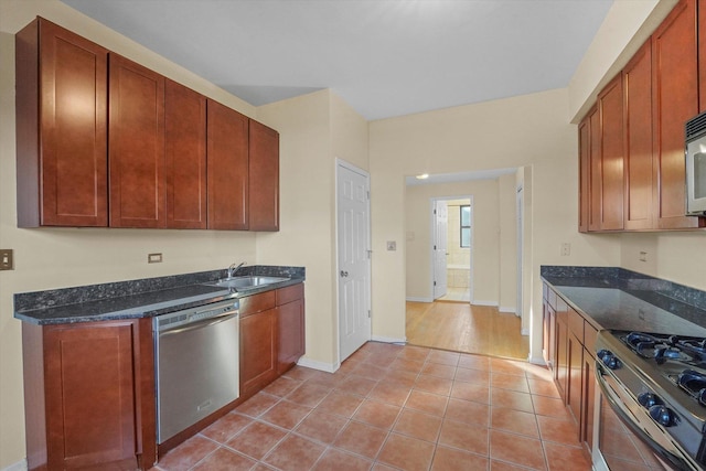 kitchen featuring baseboards, dark stone counters, light tile patterned floors, appliances with stainless steel finishes, and a sink