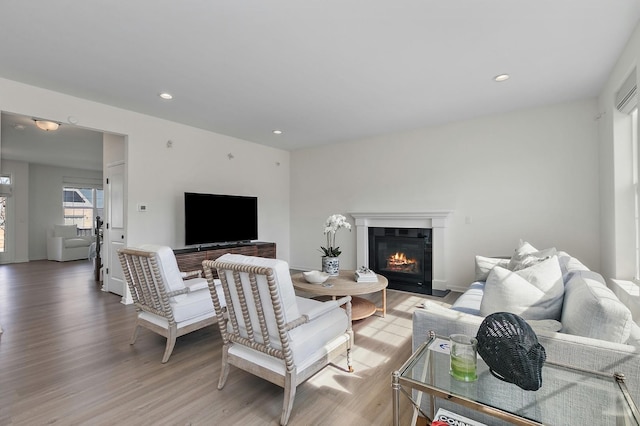 living area featuring recessed lighting, light wood-type flooring, baseboards, and a glass covered fireplace