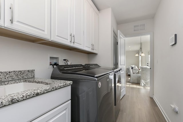 washroom with visible vents, light wood finished floors, cabinet space, washing machine and dryer, and a chandelier