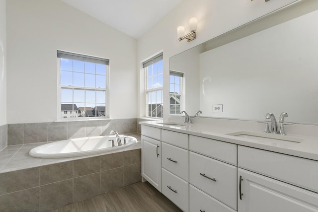 bathroom featuring a garden tub, wood finished floors, double vanity, and a sink