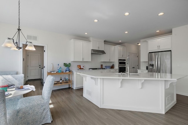 kitchen with wood finished floors, visible vents, stainless steel appliances, light countertops, and under cabinet range hood