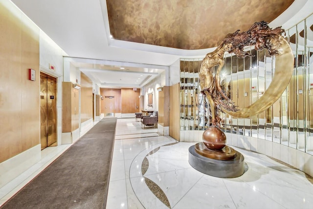 corridor with elevator, marble finish floor, and a raised ceiling