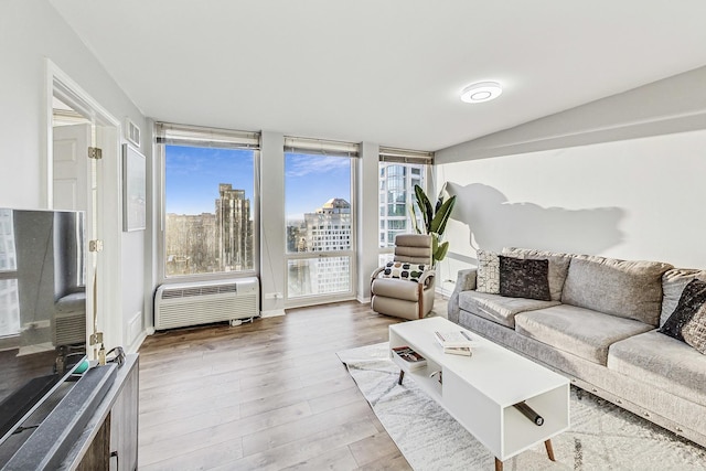 living room with a view of city, floor to ceiling windows, an AC wall unit, and wood finished floors