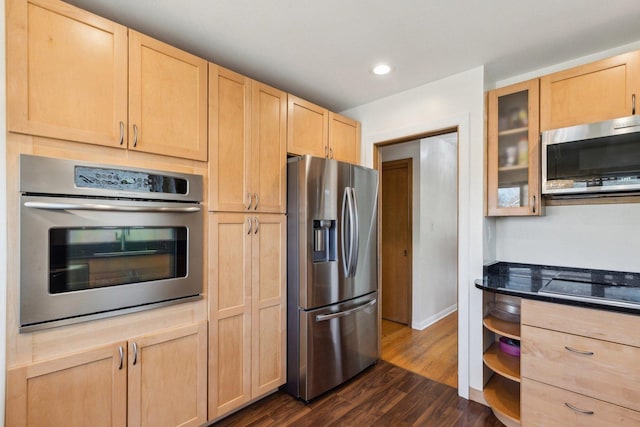 kitchen featuring light brown cabinetry, dark countertops, dark wood-style floors, appliances with stainless steel finishes, and glass insert cabinets