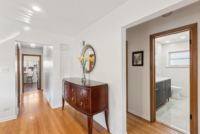 corridor with baseboards, visible vents, light wood-style flooring, recessed lighting, and a sink