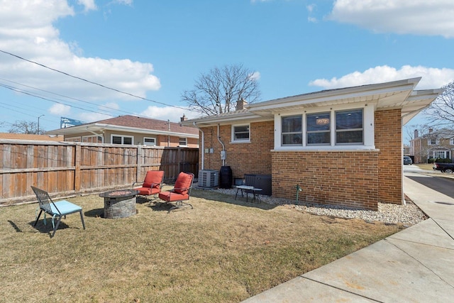 rear view of property featuring fence, cooling unit, a fire pit, and brick siding