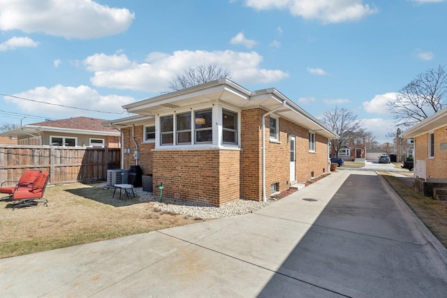 view of property exterior featuring brick siding, cooling unit, and fence