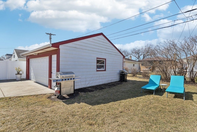 view of property exterior with a detached garage, a lawn, an outbuilding, and fence