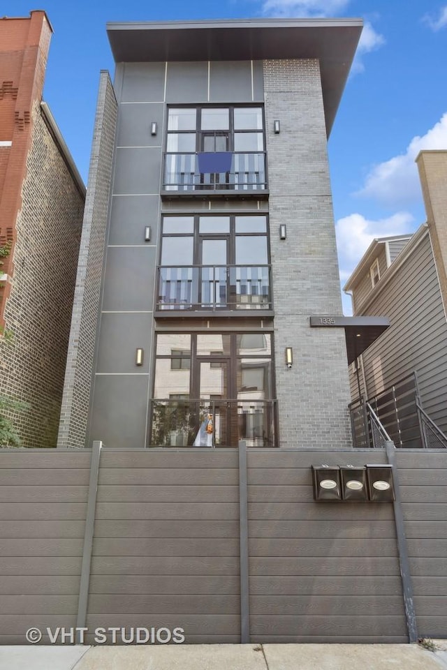 back of property with a balcony, fence, and brick siding