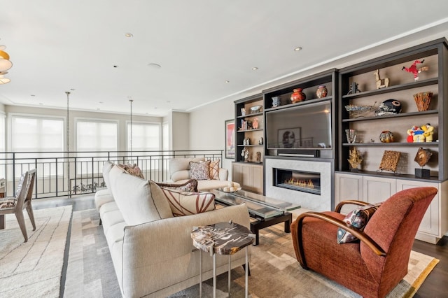 living area featuring a glass covered fireplace, recessed lighting, wood finished floors, and built in shelves