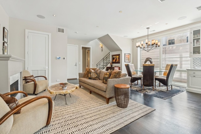 living area with visible vents, dark wood finished floors, a fireplace, a chandelier, and stairs