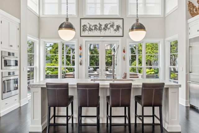 kitchen with dark wood finished floors, a high ceiling, french doors, white cabinetry, and decorative light fixtures