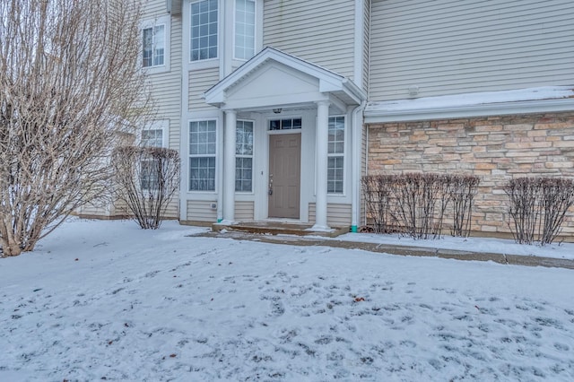 snow covered property entrance with a garage and stone siding