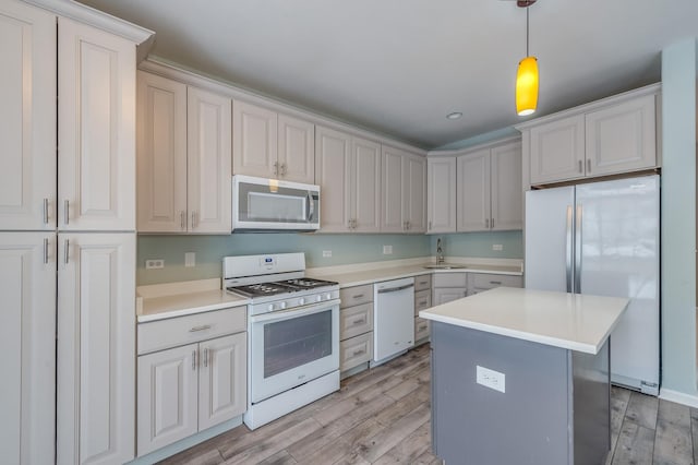 kitchen with white appliances, a sink, light countertops, decorative light fixtures, and light wood-type flooring