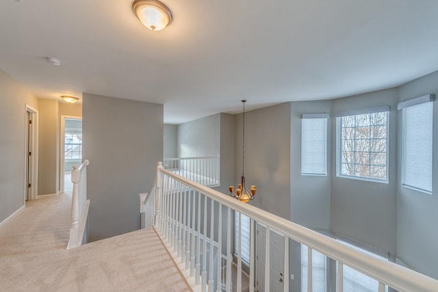 corridor with an upstairs landing, a chandelier, baseboards, and carpet