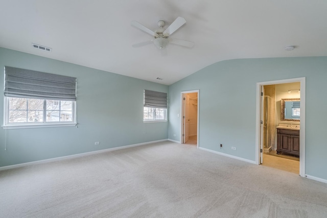 unfurnished bedroom featuring carpet, visible vents, baseboards, lofted ceiling, and a walk in closet