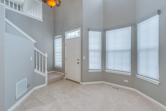 tiled entryway featuring visible vents, carpet flooring, stairs, and a towering ceiling