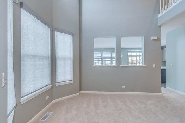 carpeted spare room with baseboards, visible vents, and a towering ceiling