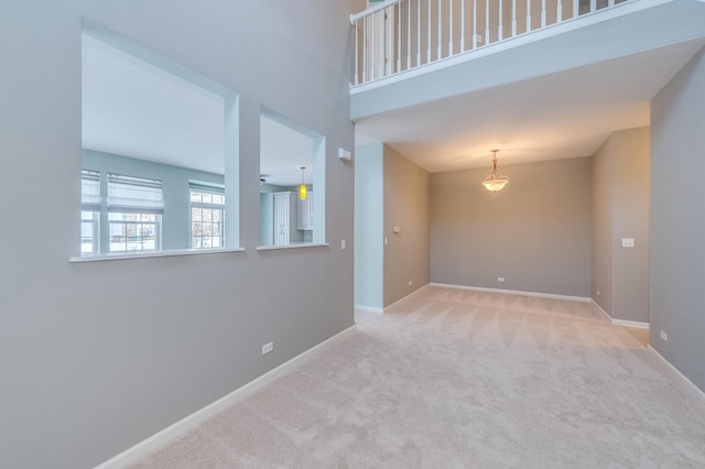 unfurnished room featuring baseboards, a towering ceiling, and carpet flooring