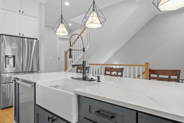 kitchen featuring pendant lighting, light stone countertops, appliances with stainless steel finishes, and a sink