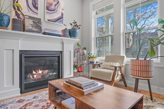 living area with a glass covered fireplace, baseboards, and wood finished floors