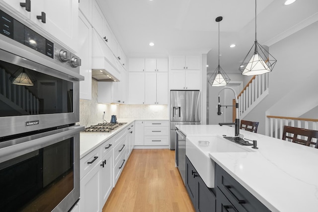 kitchen featuring stainless steel appliances, hanging light fixtures, white cabinets, light wood-style floors, and backsplash