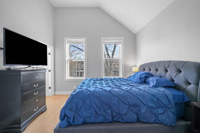 bedroom with lofted ceiling, baseboards, and light wood finished floors