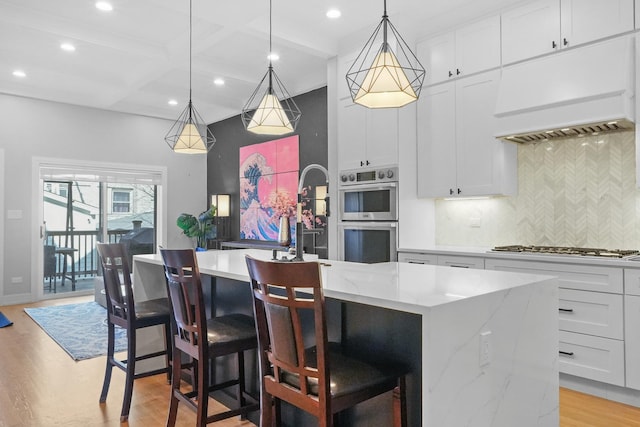 kitchen with premium range hood, coffered ceiling, a center island, stainless steel double oven, and light wood-style floors