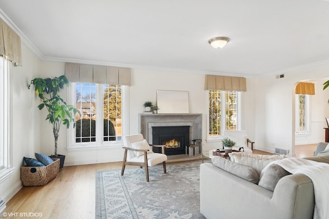 living room featuring visible vents, wood finished floors, arched walkways, a lit fireplace, and crown molding