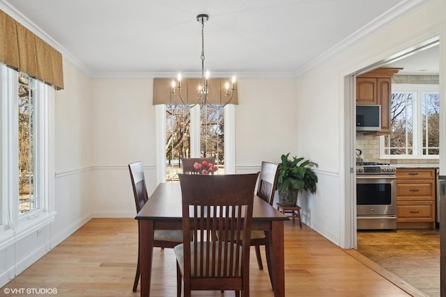 dining area with light wood-style flooring, a notable chandelier, baseboards, and ornamental molding