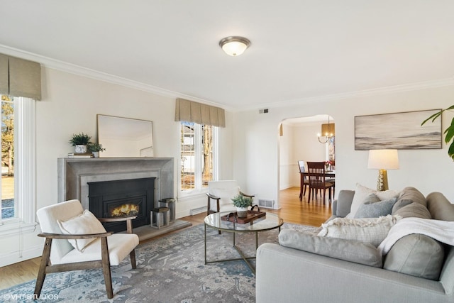 living area with wood finished floors, visible vents, arched walkways, a warm lit fireplace, and crown molding