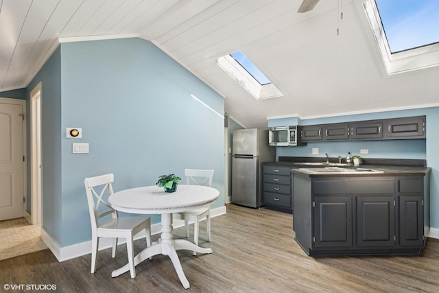 kitchen featuring lofted ceiling with skylight, a peninsula, appliances with stainless steel finishes, and wood finished floors