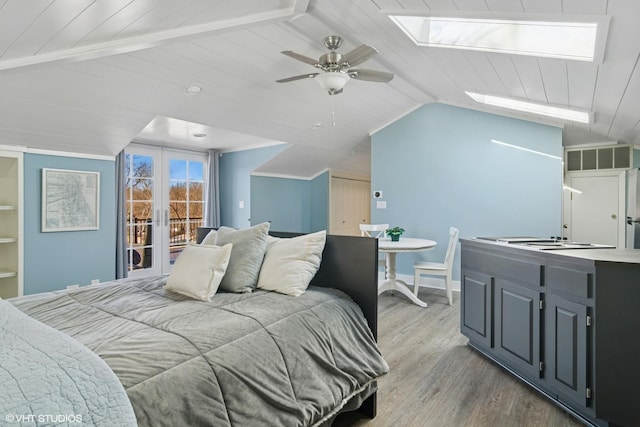 bedroom with a ceiling fan, wood finished floors, vaulted ceiling with skylight, french doors, and access to outside