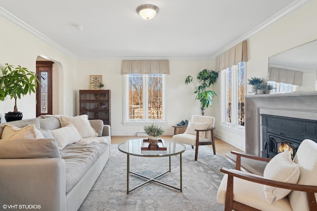 living area featuring wood finished floors, arched walkways, a glass covered fireplace, and ornamental molding